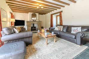 A cozy living room with a fireplace, leather sofas, a wooden coffee table, and a patterned rug. - 3 Bed in Bodmin (oc-ltbra) (Cardinham)