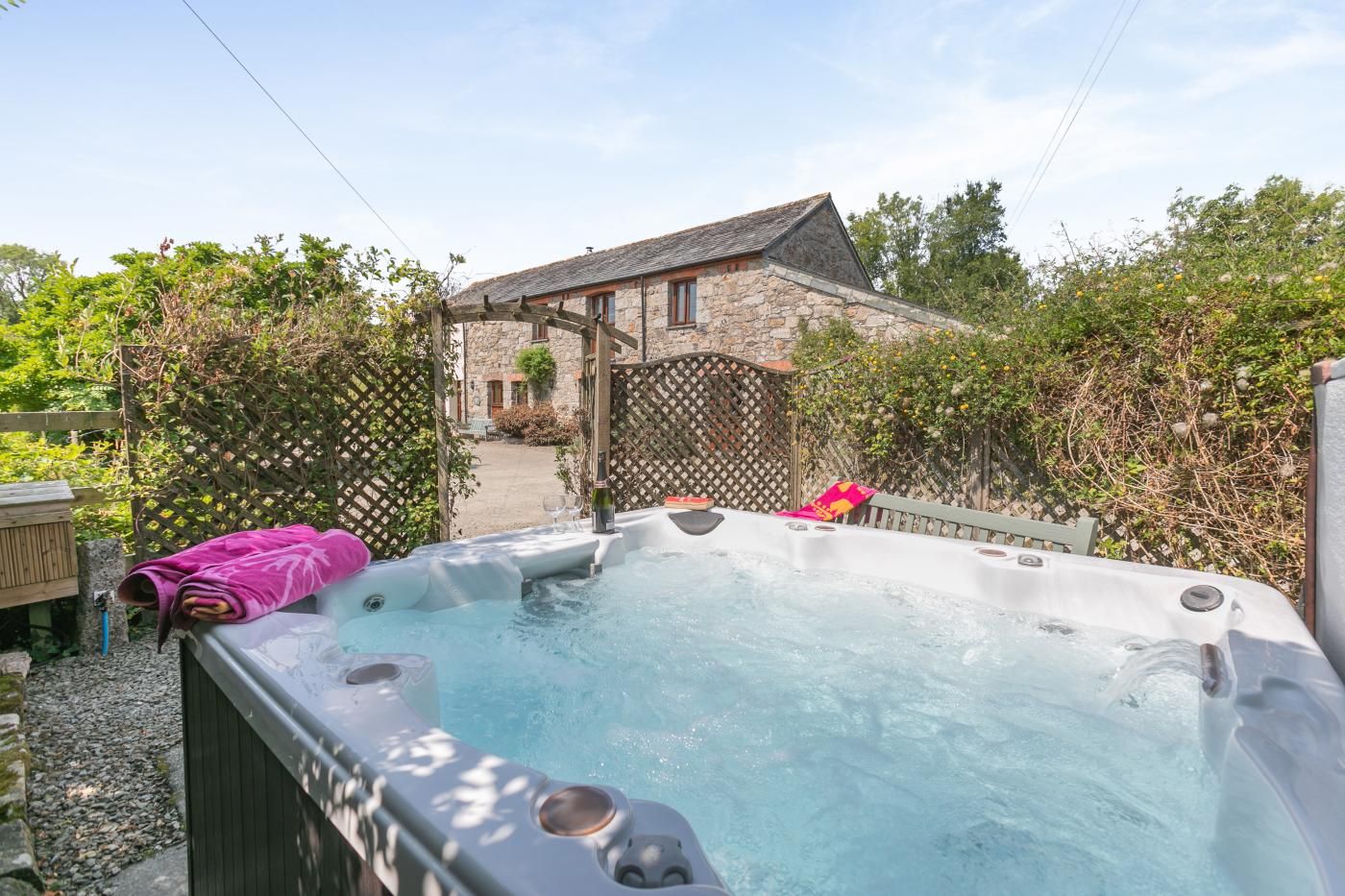 A hot tub with a stone wall and a wooden fence in a garden setting.