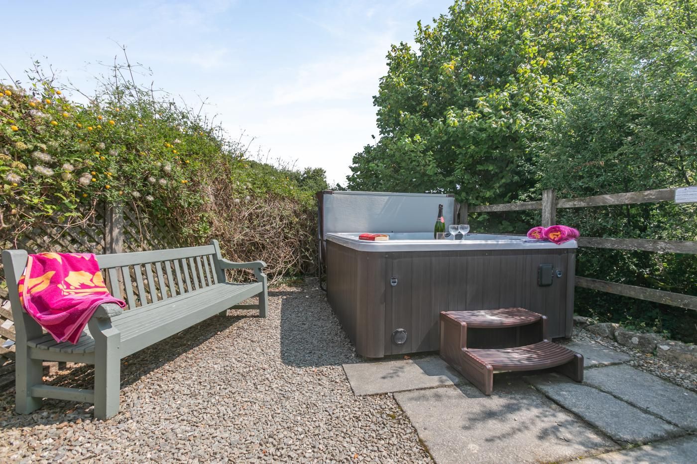 A hot tub with a wooden deck, a bench with a pink towel, and a wooden fence.