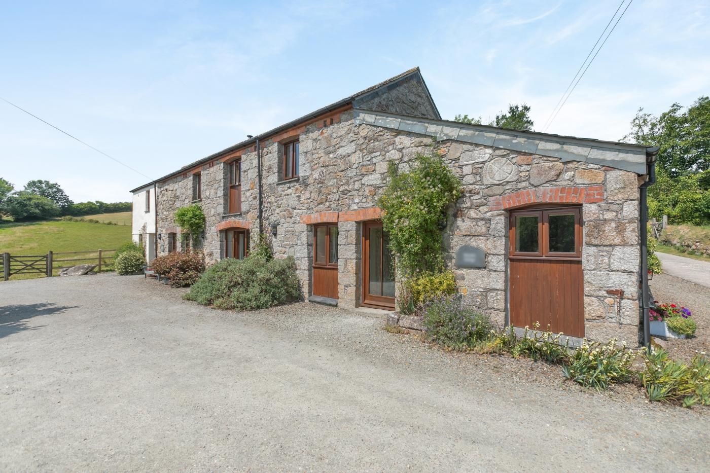 A stone building with a gravel driveway, wooden doors, and a fenced property.