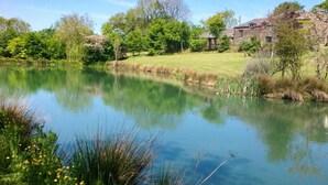 A serene pond with surrounding greenery and a stone building in the background. - 4 Bed in Holsworthy (oc-lamer) (Holsworthy Hamlets)