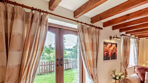 A room with a wooden ceiling, a sliding glass door leading to a garden, a small table with a vase of flowers, and a red sofa. - 4 Bed in Holsworthy (oc-lamer) (Holsworthy Hamlets)