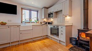 Una cucina moderna con mobili bianchi, forno a incasso, microonde e stufa a legna.