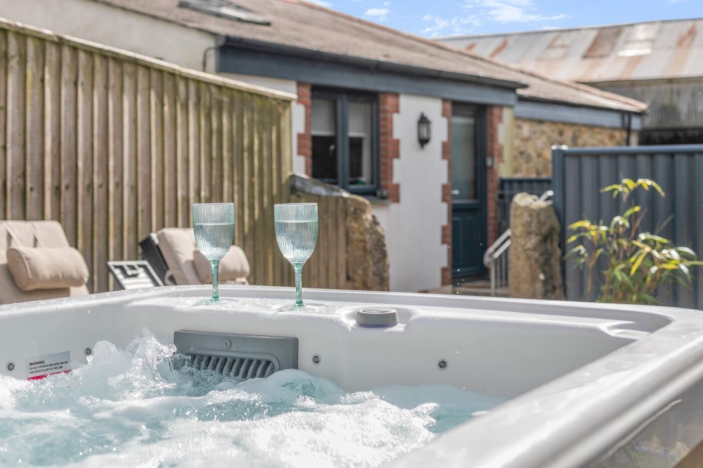 Un jacuzzi con dos vasos, una cerca de madera y una casa al fondo.