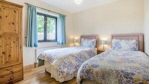 Ein Schlafzimmer mit zwei Betten, einem Holzschrank, einem Fenster mit Vorhängen und einer Pendelleuchte.