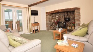A living room with a stone fireplace, a television, and a sofa. - 3 Bed in Bideford (oc-glake) (Hartland)