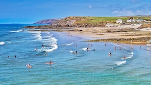 A coastal beach scene with waves, people swimming and surfing, and houses in the background. - 3 Bed in Bideford (oc-glake) (Hartland)