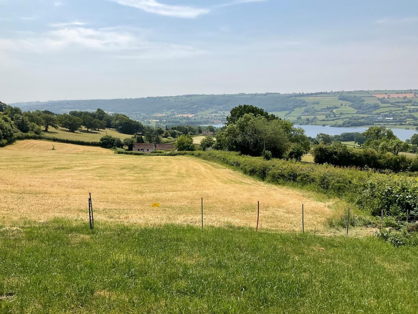 Ländliche Landschaft mit einem Feld, einem Zaun und weiter Wasserfläche.