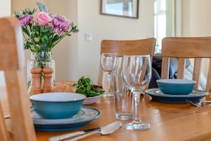 Ein Esstisch ist gedeckt mit blauen Tellern, Schüsseln und Besteck, dazu ein Blumenstrauß und ein Salat.