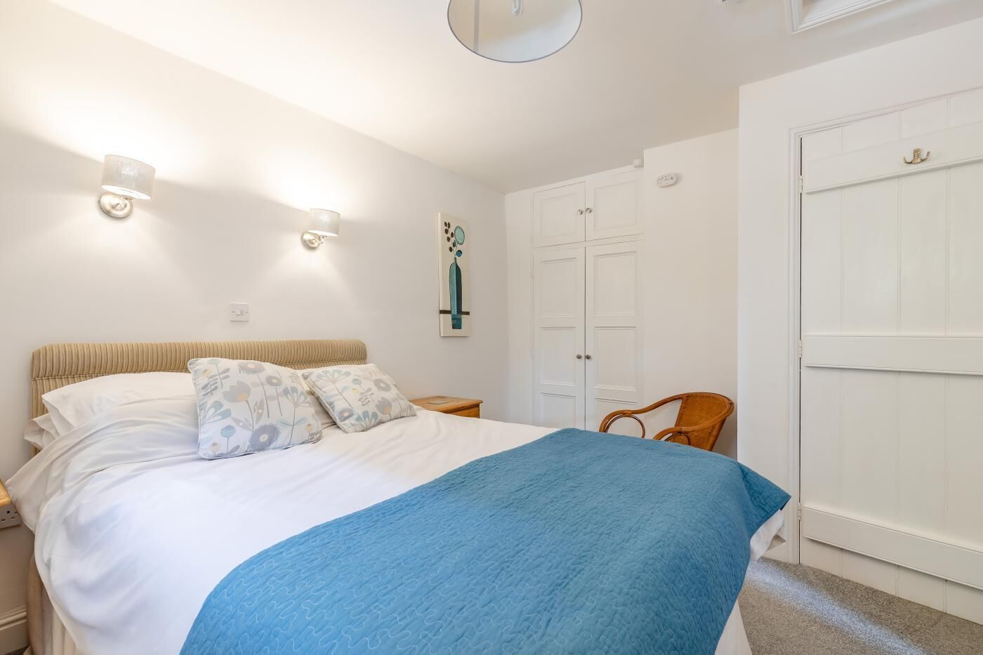 Quarto com cama, mesas de cabeceira, guarda-roupa e luminária na parede.