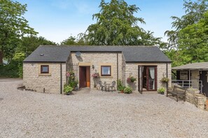 A stone building with a gravel driveway, a wooden door, and a small outdoor seating area with a bench and table. - 1 Bed in Hope Valley (oc-pk849) (Bradwell)