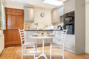 A modern kitchen with white cabinetry, a round dining table, and two chairs. - 1 Bed in Hope Valley (oc-pk849) (Bradwell)