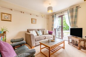 A living room with a sofa, two chairs, a coffee table, a television on a wooden stand, and a large window with curtains. - 1 Bed in Hope Valley (oc-pk849) (Bradwell)