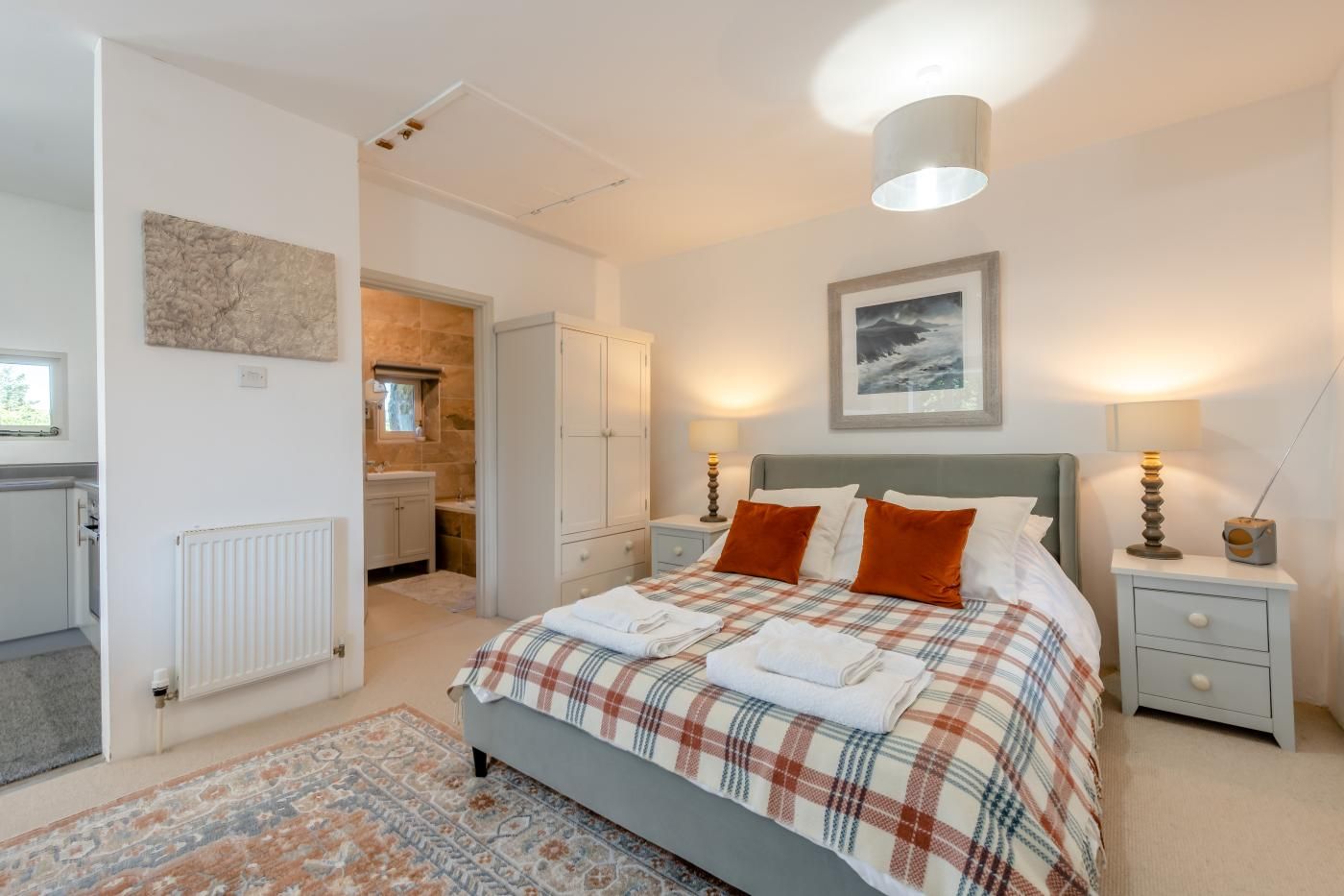 A bedroom with a bed, nightstands, a radiator, a window, and a door leading to a bathroom.