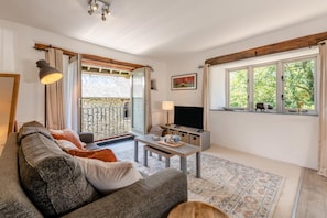 A cozy living room with a sofa, a TV, and a balcony with a view of greenery. - 1 Bed in Tavistock (oc-highm) (Cudlipptown)