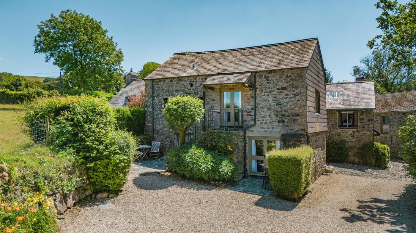 A stone building with a gravel driveway, a small patio with a table and chairs, and a well-maintained garden.