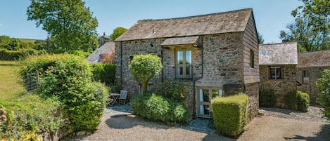 A stone building with a gravel driveway, a small patio with a table and chairs, and a well-maintained garden.