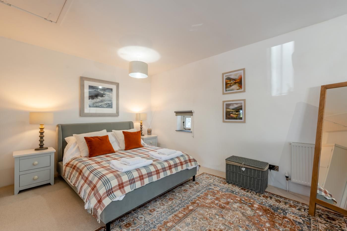 A bedroom with a bed, nightstands, a dresser, a radiator, and a window.