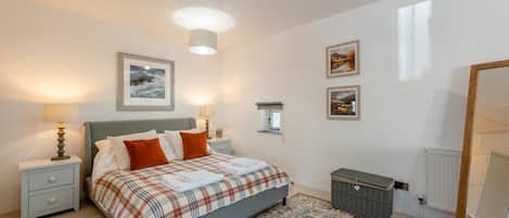 A bedroom with a bed, nightstands, a dresser, a radiator, and a window.
