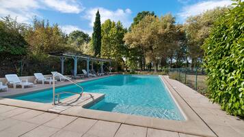Une piscine rectangulaire, bordée d’une terrasse carrelée et entourée de verdure et d’arbres.