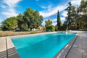 A rectangular swimming pool with clear blue water, surrounded by a tiled deck and a metal fence.