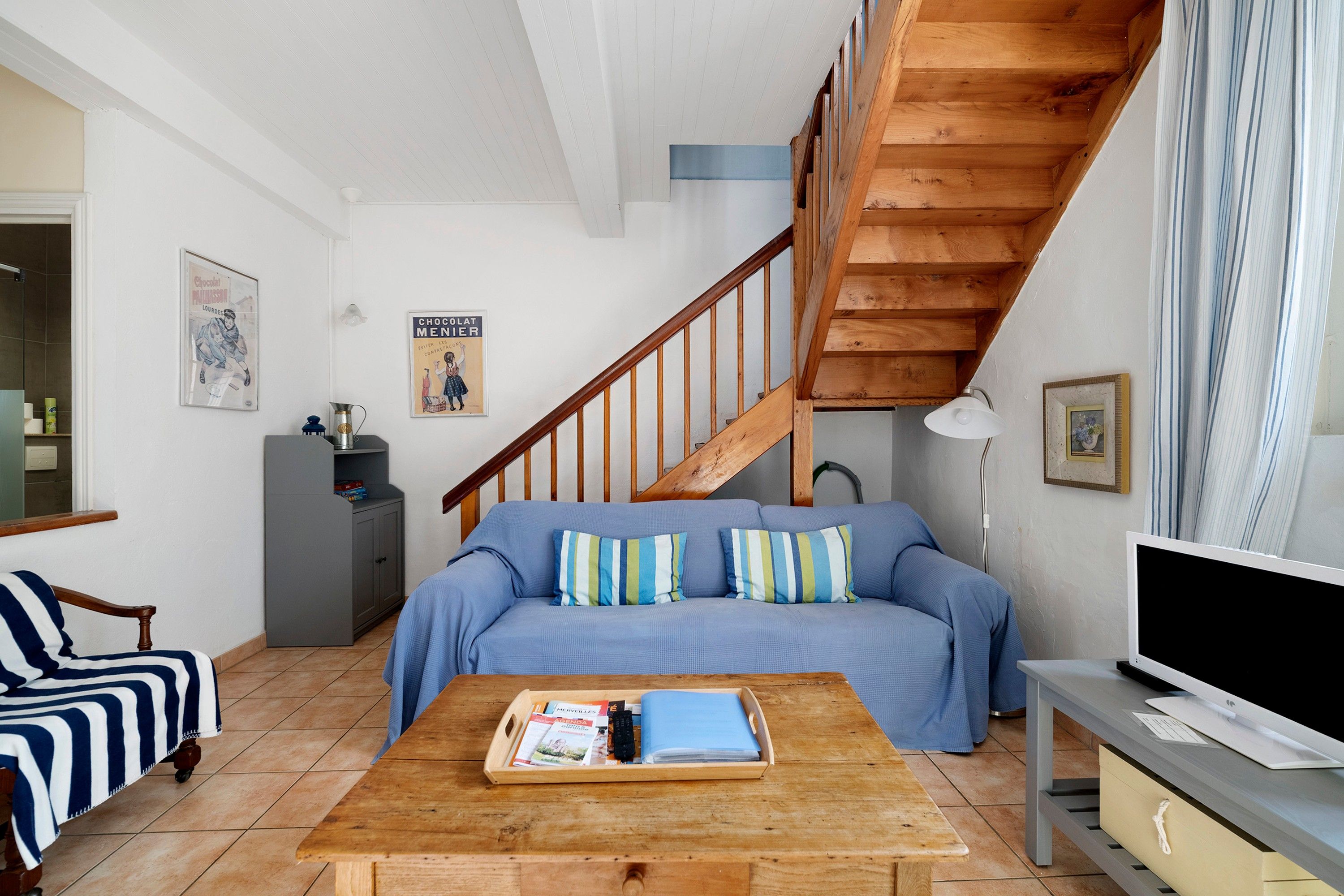 Una sala de estar con un sofá, una mesa de centro de madera, un televisor, una escalera y un armario.