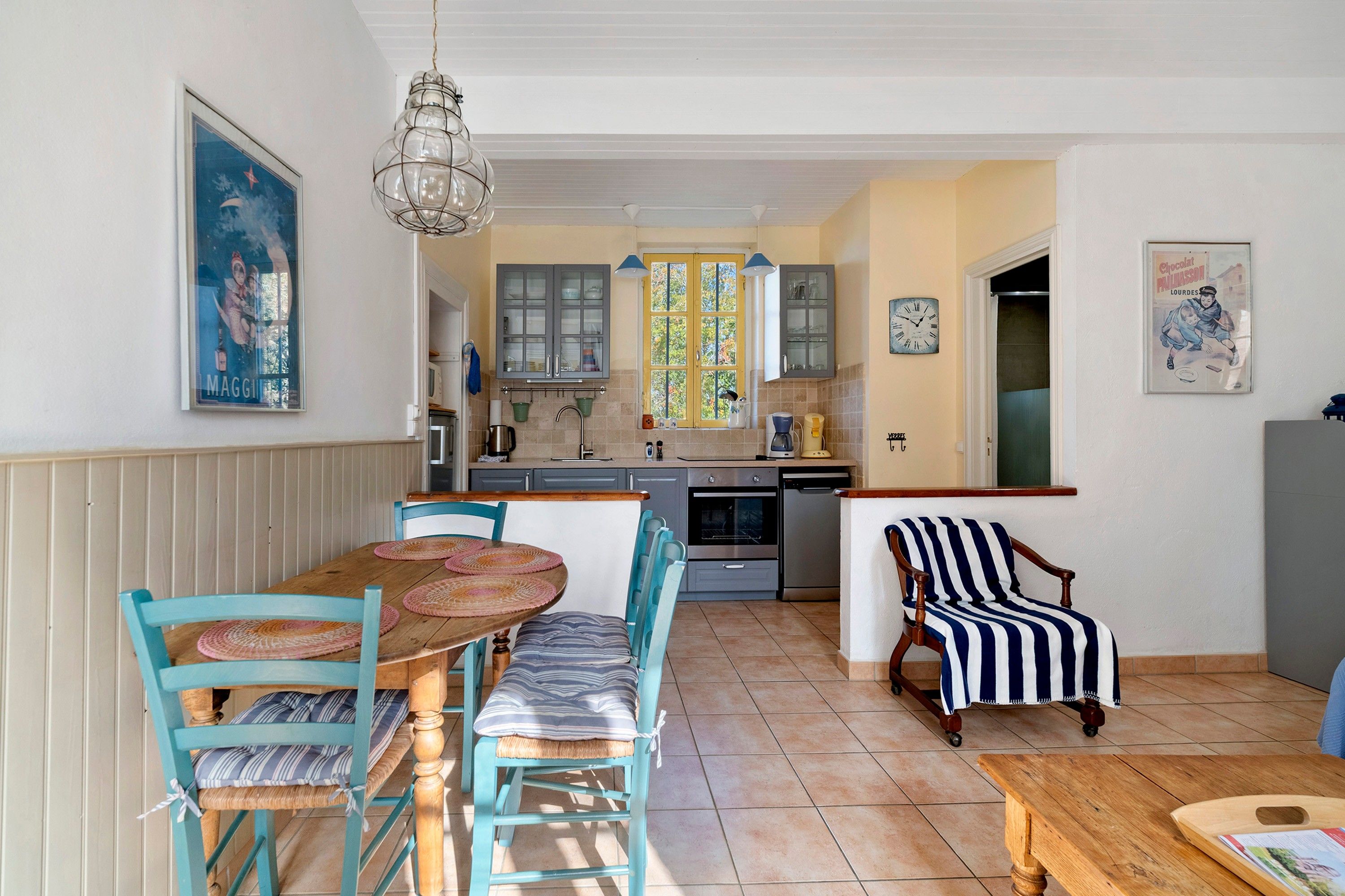 Une cuisine chaleureuse avec un coin repas, comprenant une table en bois, des chaises et un fauteuil à rayures.
