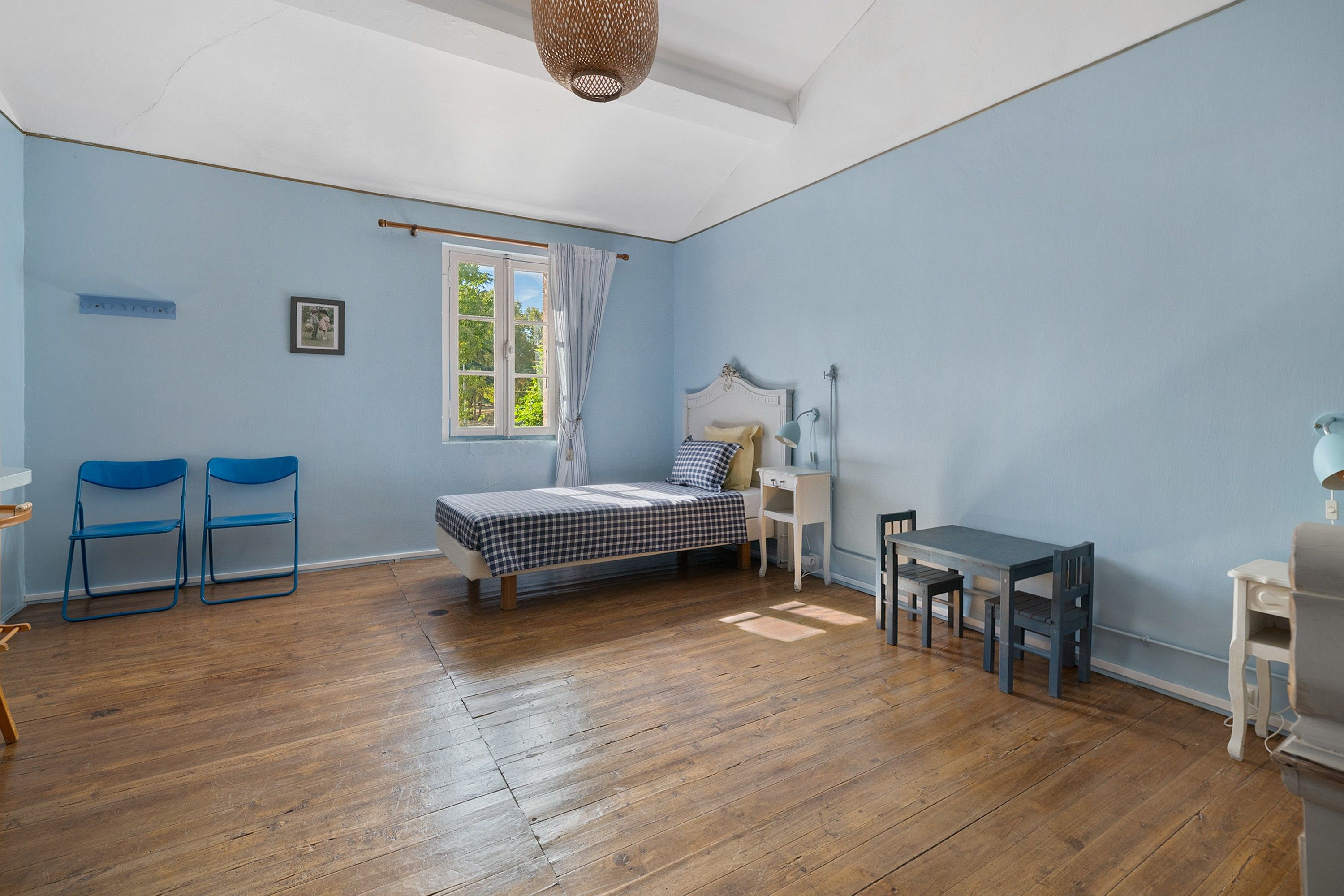 Une pièce comprenant un lit, un bureau, deux chaises, une fenêtre et un luminaire suspendu.
