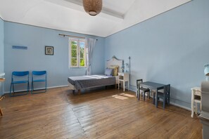 Une pièce comprenant un lit, un bureau, deux chaises, une fenêtre et un luminaire suspendu.