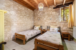 Une chambre rustique avec deux lits en bois, des murs en pierre, un plafond en bois et une fenêtre avec des rideaux.