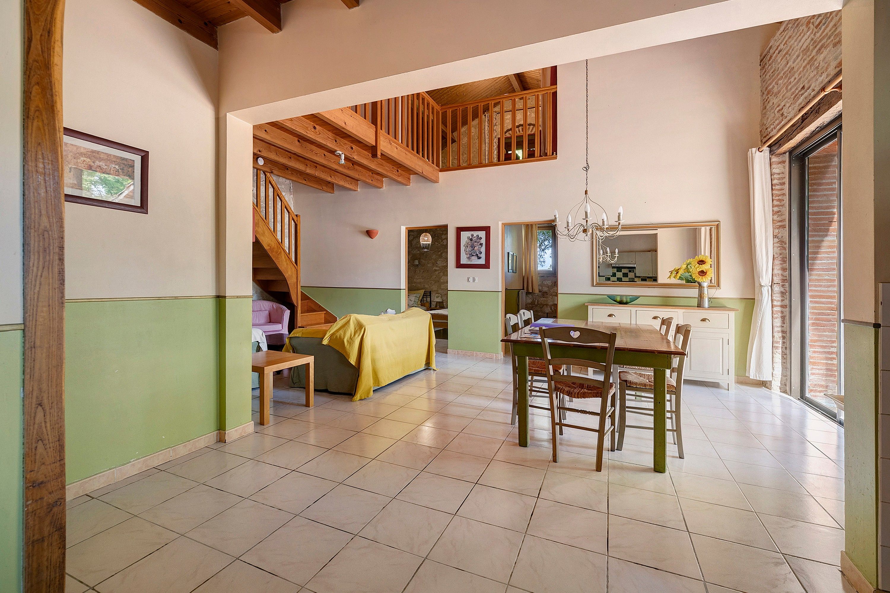 A spacious dining area with a wooden table and chairs, a staircase leading to an upper level, and a kitchen with a large window.