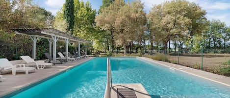A rectangular swimming pool with clear blue water, surrounded by lounge chairs and a pergola.