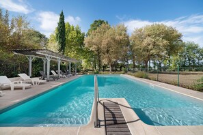 Una piscina rectangular con agua azul cristalina, rodeada de sillones de descanso y una pérgola.