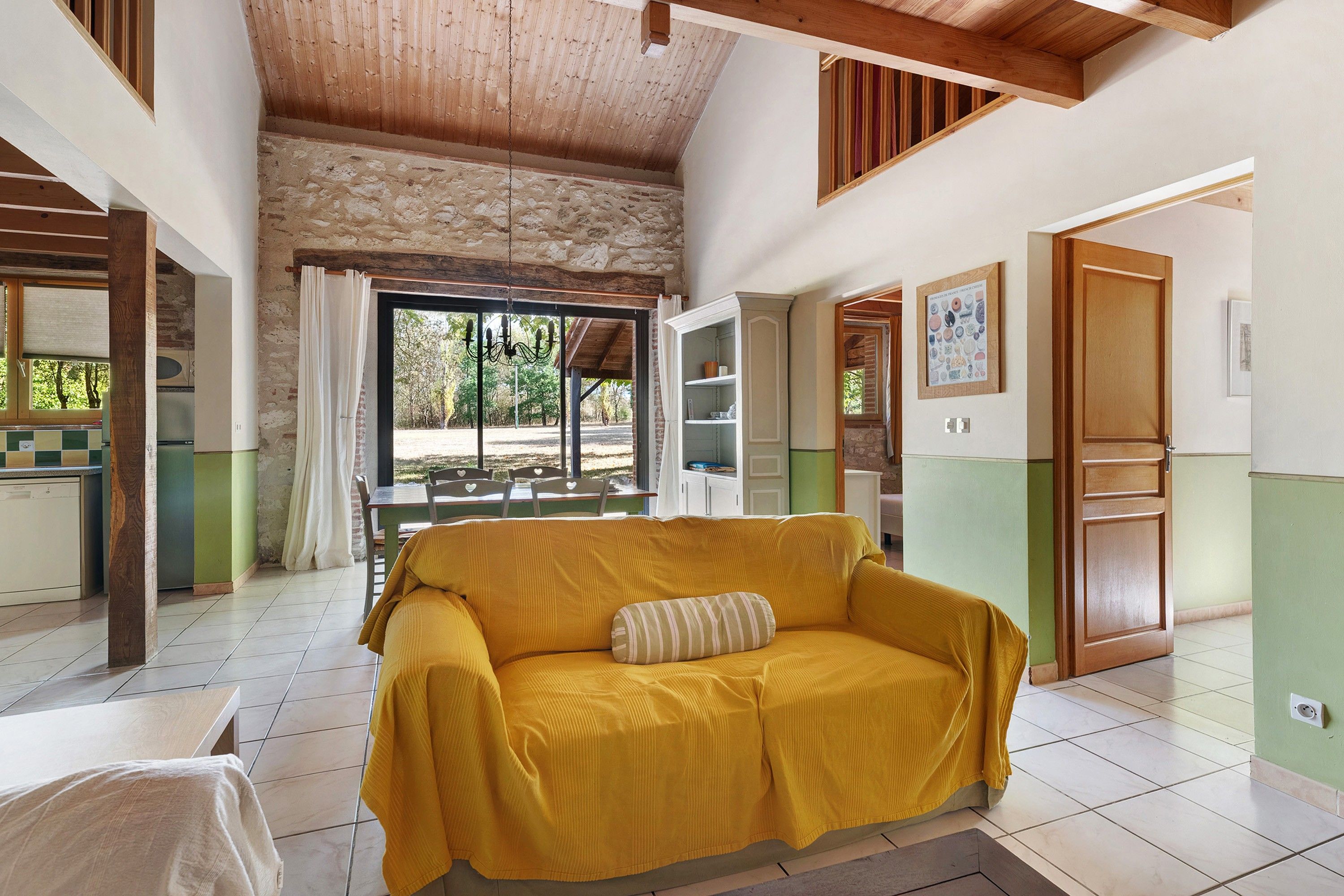 Una habitación con un sofá amarillo, una zona de comedor con sillas, una cocina y vistas a través de una ventana.