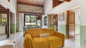 Una habitación con un sofá amarillo, una zona de comedor con sillas, una cocina y vistas a través de una ventana.