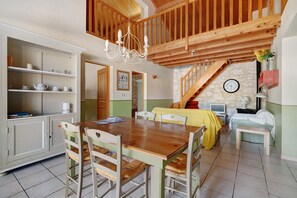 Un comedor amplio con una mesa y sillas de madera, una cocina con armarios blancos y una escalera que lleva a un nivel superior.
