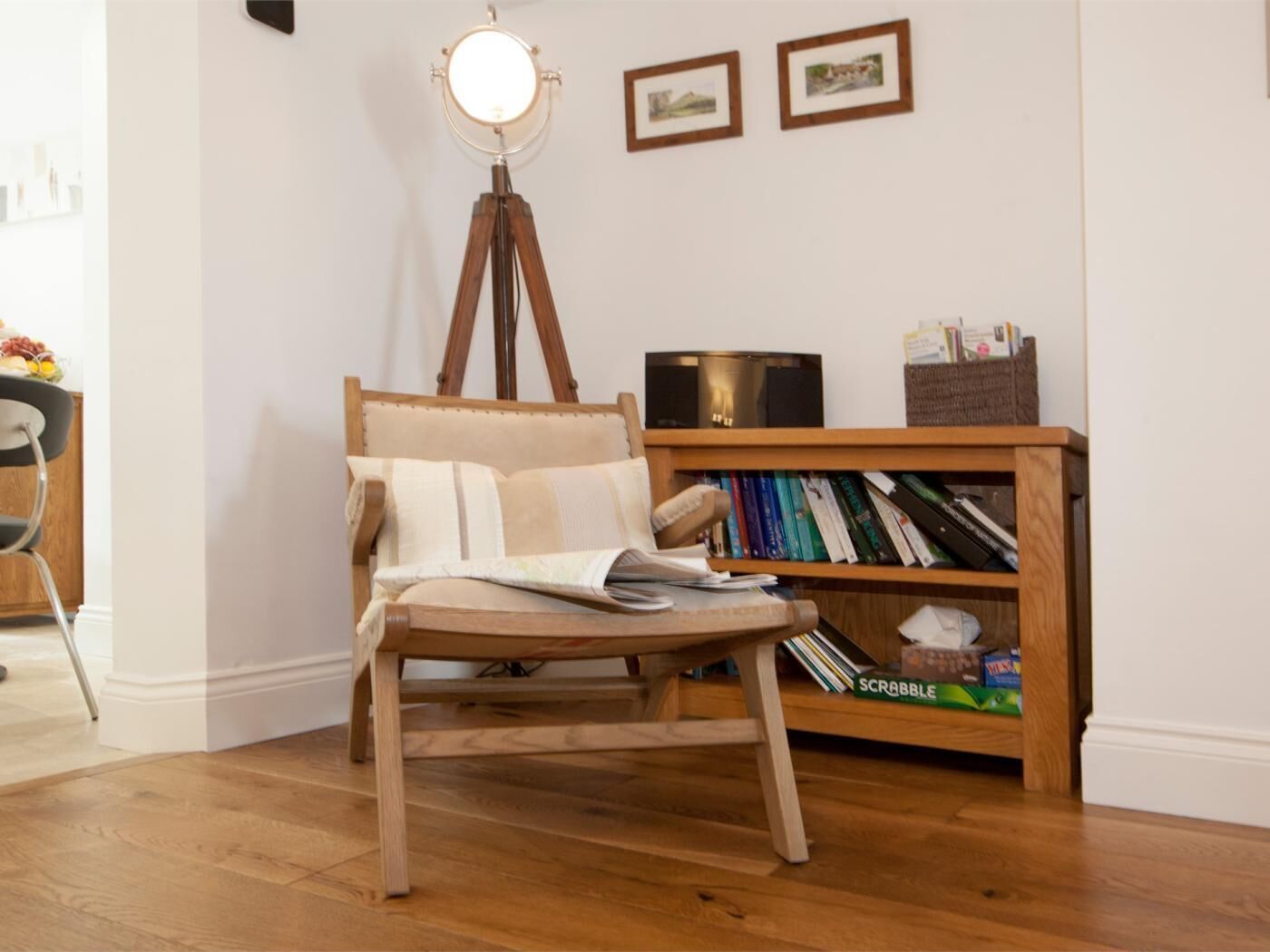 Een houten stoel met een kussen, een vloerlamp en een boekenplank vol boeken en spellen.