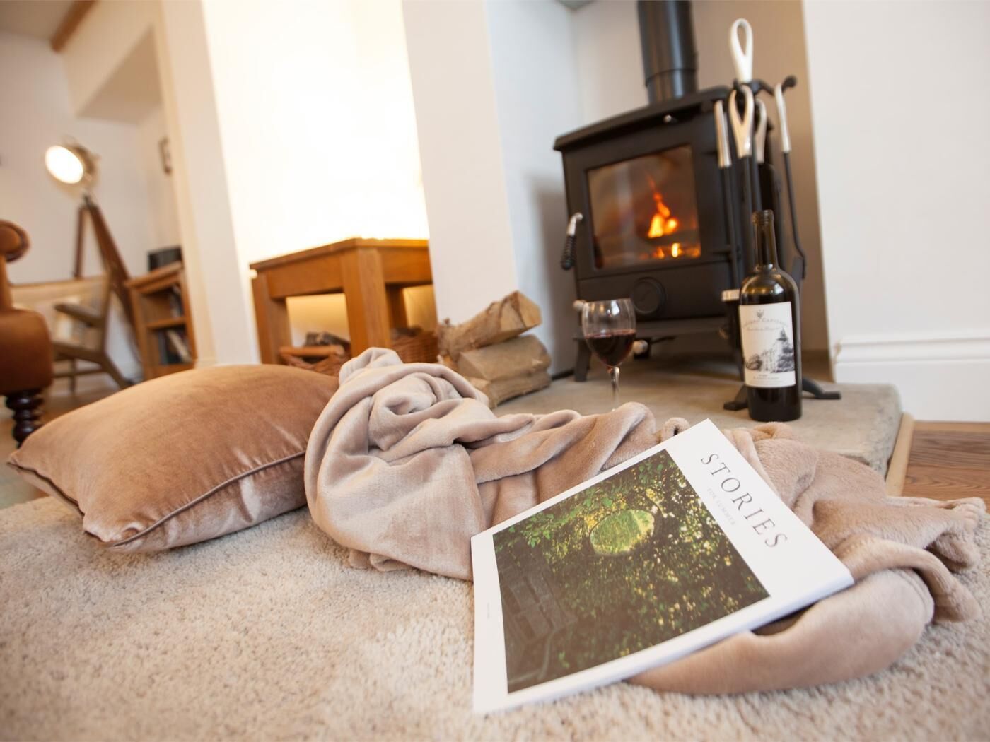 Een gezellige woonkamer met een open haard, een fles wijn en een boek getiteld 'STORIES'.