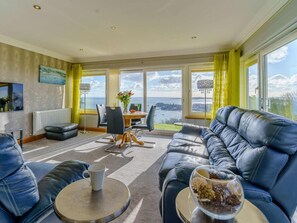 Ein modernes Wohnzimmer mit einer Couch, einem Esstisch und Meerblick.
