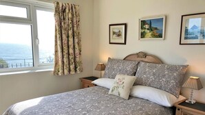 Een slaapkamer met een bed, twee nachtkastjes, een raam met gordijnen, en drie afbeeldingen in lijsten aan de muur.