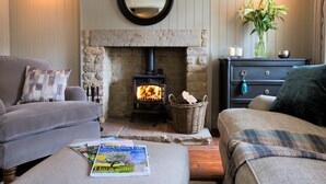 Ein gemütliches Wohnzimmer mit Kamin aus Stein, zwei Sofas, einem Couchtisch mit Zeitschriften und einem dekorativen Spiegel an der Wand.