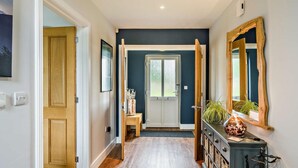 Un couloir avec un plancher en bois, une porte, un banc, un miroir et un meuble.