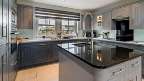 Une cuisine moderne avec des meubles de couleur sombre, un îlot central et une grande fenêtre offrant une vue sur l’extérieur.