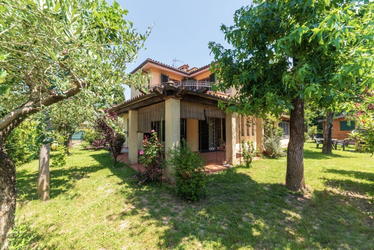 Une maison à deux étages dotée d’un balcon, entourée d’un jardin bien entretenu et d’arbres.
