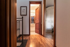A hallway with wooden flooring, a staircase with black balusters, and a white door leading to a kitchen area.