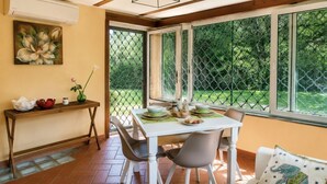 Een eethoek met een tafel, stoelen, een bank en uitzicht door een raam met hor.
