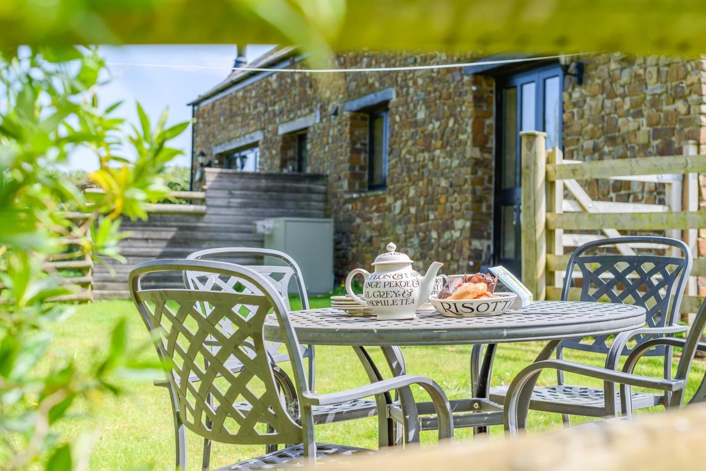 A stone building with a door, a table with chairs, a teapot, and a plate with food.