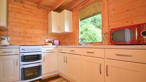 Una cocina con paredes de madera, muebles blancos, un microondas rojo y una ventana con vista a follaje.