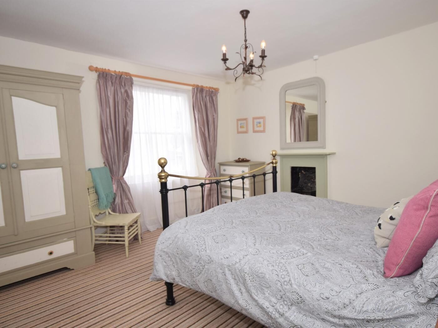 A bedroom with a bed, a chair, a dresser, a mirror, and a fireplace.