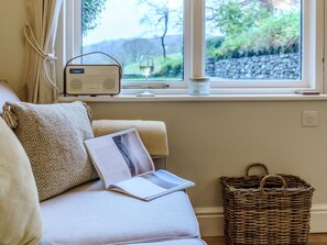 Ein gemütliches Zimmer mit Fenster, einem Radio, einem Glas Wein, einem Korb und einem Buch.
